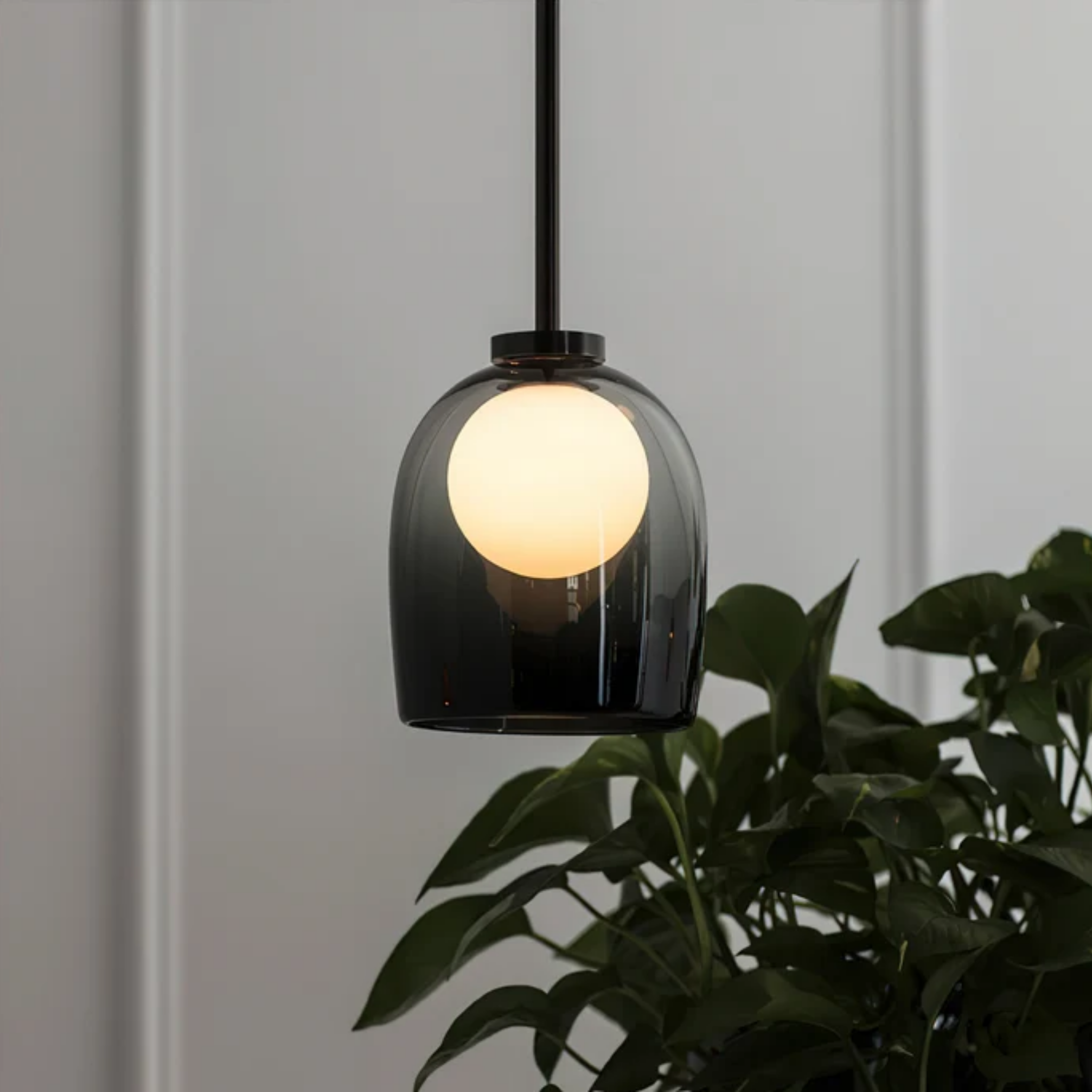 Modern smoke gray glass bell pendant ceiling light beside a wall and potted plant
